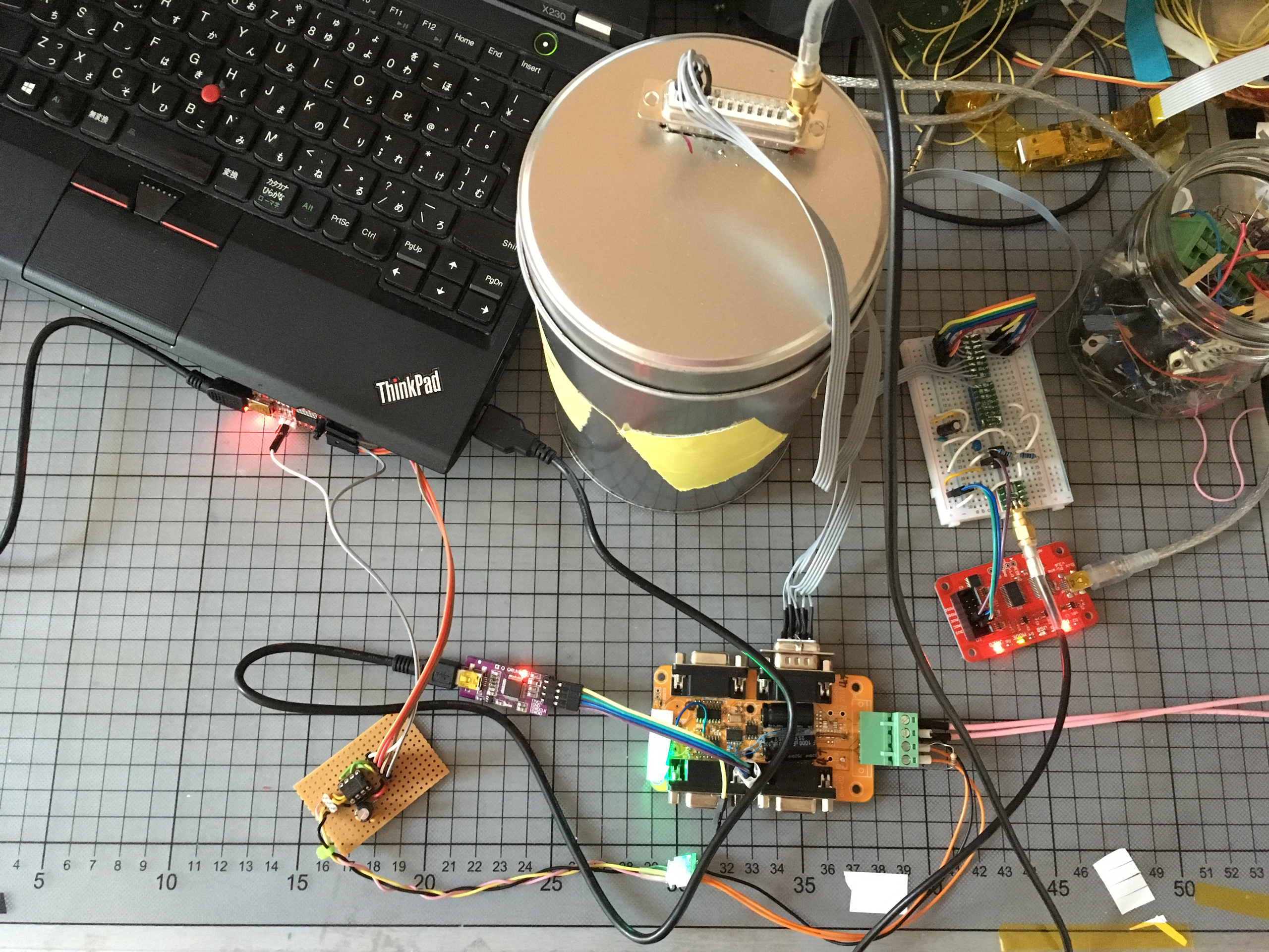The led measurement setup consists of several PCBs and a
    breadboard linked with a bunch of wires and a big tin can to shield the LEDs and the photodiode. A large sub-D
    connector is put into the top of the tin can as a feed-through for the LED tape's control signals and the
    photodiode signal. In the background the control laptop is visible.